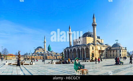 Die lokale Mensch in grüne Tracht auf dem zentralen Platz mit dem Mevlana Museum und die Selimiye-Moschee im Hintergrund Stockfoto