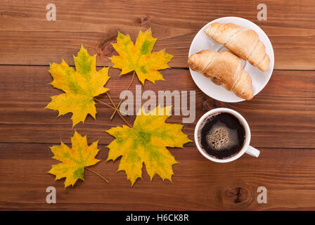 Kaffee, Gipfeli und Ahorn Blätter auf hölzernen Hintergrund. Stockfoto