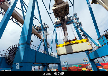 Ein massive Fracht Kran transportiert einen Container von einem LKW auf einem Frachter Schiff in einem Hafen Dock. Stockfoto