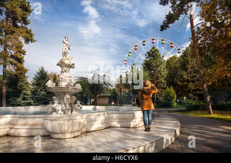 Frau mit Hut in der Nähe von Brunnen mit Statuen betrachten Riesenrad im Herbst park Stockfoto