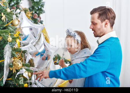 Tochter und Vater schmücken den Weihnachtsbaum. Vater Tochter unterstützt und kleine süße Mädchen hängt an den Weihnachtsbaum-Spielzeug. Stockfoto