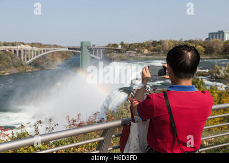 Ein Tourist nutzt eine Smartphone, um ein Foto von den American Falls und die Niagara River aus Luna Island in Niagara Falls, New York zu fangen. Stockfoto