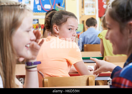 Unglückliche Mädchen wird getratscht über durch Schulfreunde im Klassenzimmer Stockfoto