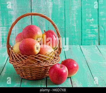 Reife rote Äpfel in einem Korb auf einem hellen Hintergrund aus Holz. Stockfoto