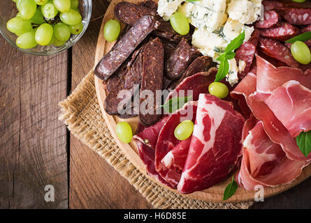 Antipasti-Platte mit Speck, Dörrfleisch, Wurst, Blauschimmelkäse und Trauben auf einem hölzernen Hintergrund catering. Ansicht von oben Stockfoto