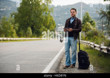 Mann, stehend mit digital-Tablette warten auf dem Auto oder Taxi. Trampen Stockfoto