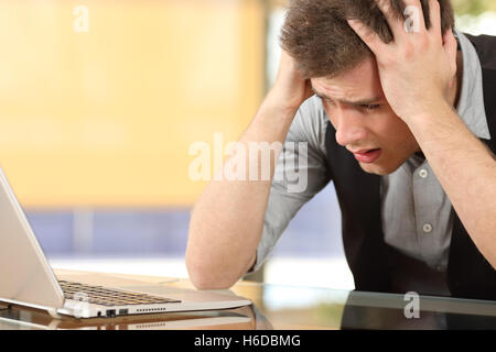 Nahaufnahme eines besorgt Unternehmers gerade Laptop mit den Händen auf dem Kopf sitzen in einem Schreibtisch in einem Büro indoor Stockfoto