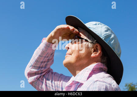 Eine ältere Frau mit einem breiten Sonnenhut und Sonnenbrille im Sonnenschein Krempe Schattierungen ihre Augen weit bis in die Sonne zu schauen im Sommer. England Großbritannien Großbritannien Stockfoto