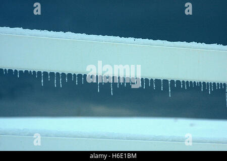 Kleine zarte Eiszapfen auf weißen Zaun Stockfoto