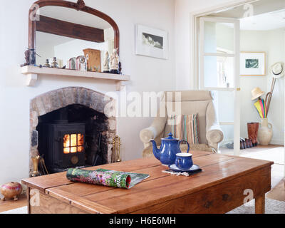 Ein Tisch mit einer Zeitschrift, Teekanne & Teetasse in einem komfortablen Land Wohnzimmer mit Holzofen. de Stockfoto