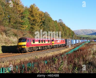 Zwei Klasse 90 e-Loks auf der West Coast Main Line in der Nähe von Beckfoot in Cumbria mit einem Güterzug von Containern. Stockfoto