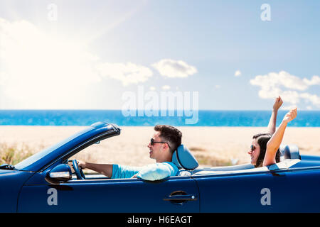 Porträt des jungen Mannes blau Cabrio fahren hautnah. Freundin sitzt auf der Rückseite die Arme in die Luft. Stockfoto