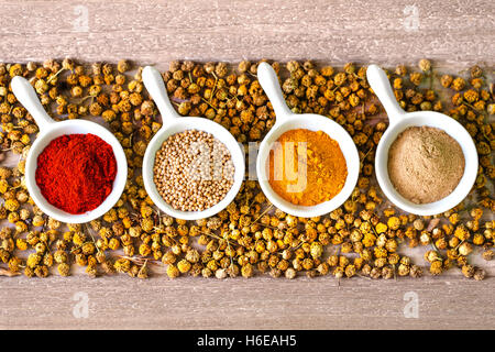 Draufsicht der vier Keramikschalen mit aromatischen Kräutern und Samen auf Bett aus getrocknete Kamillenblüten. Kopieren Sie Raum auf Ober- und Unterseite. Stockfoto