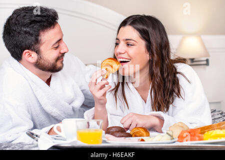 Porträt der Paare, die Spaß beim Frühstück im Hotelzimmer hautnah. Mädchen zu Bissen von Croissant nehmen. Stockfoto