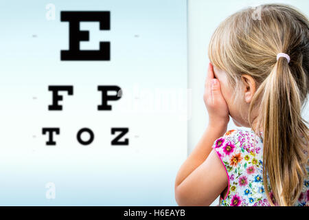 Heckansicht des Mädchen testen Sehkraft hautnah. Kleinkind schließen ein Auge mit der Hand Vision Test-Chart betrachten. Stockfoto