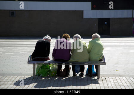 vier Omas mit Zwillingen auf einer Bank Klatsch von hinten mit Einkaufstüten sitzen Stockfoto