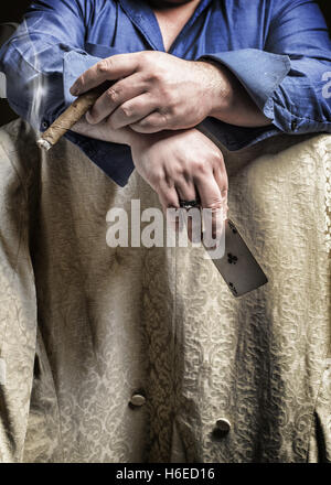 Mann sitzt rittlings auf einen Stuhl, eine Zigarre rauchend und halten ein Ass-Spielkarten Stockfoto
