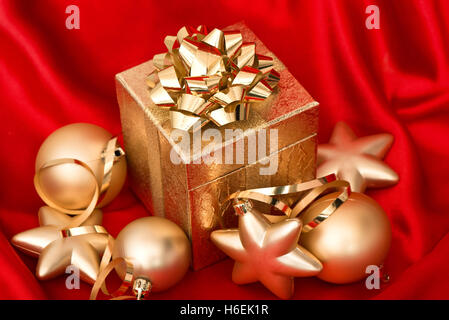 Geschenkbox mit goldenen Weihnachtskugeln auf rote Seide Hintergrund. Festliche Dekoration Stockfoto