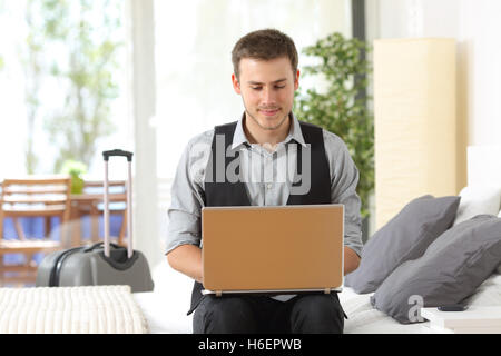 Vorderansicht Porträt eines Geschäftsmannes arbeiten auf Linie mit einem Laptop sitzt in einem Bett eines Hotelzimmers während einer Geschäftsreise Stockfoto