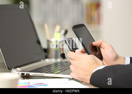 Nahaufnahme von einem executive Hände Synchronisierung eine Smartwatch und ein Telefon in einem Schreibtisch im Büro mit einem Laptop im Hintergrund Stockfoto
