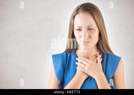 Frau mit einer Halsentzündung halten ihren Hals, isoliert in grau Stockfoto