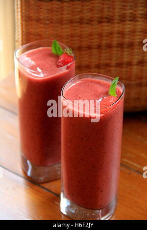 Zwei köstliche Frucht-Smoothies in hohen Gläsern garniert mit Minzblättern und Erdbeeren, auf Holztisch gesetzt für die Menschen zu genießen. Stockfoto