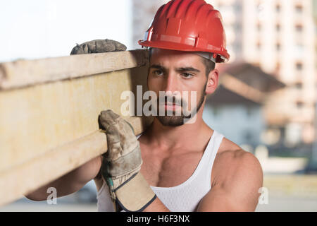 Tischler tragen einen großen Holzbohle auf seine Schulter lächelnd Stockfoto