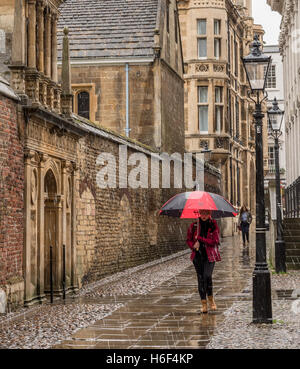 Junge Frau wandern in Heavy Rain mit Regenschirm in Cambridge, in der Nähe von Historic college Gebäude Stockfoto