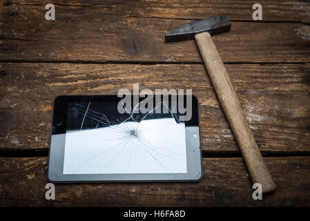 Hammer und Tablet auf dem Holztisch mit Glasscherben. Stockfoto