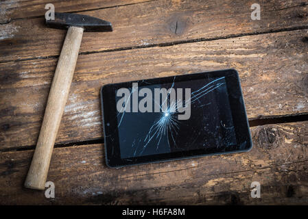 Hammer und Tablet auf dem Holztisch mit Glasscherben. Stockfoto