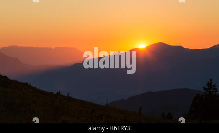 Die Sonne geht hinter den Bergen und färbt den Himmel orange. Stockfoto