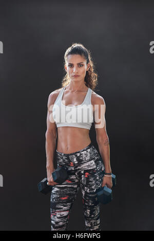 Fitness-Frau mit Hanteln trainieren. Schöne Fitnesstrainer auf schwarzem Hintergrund. Weibliches Modell mit muskulösen Passform und sl Stockfoto