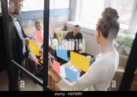 Geschäftsleute mit einem Treffen im Büro. Frau stand vor der Glaswand mit post-it Notes und erklären Unternehmen ide Stockfoto