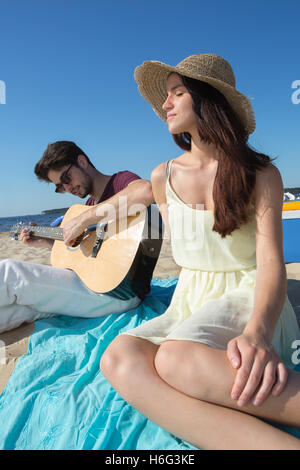 junger Mann mit seiner Gitarre und Freundin am Strand Stockfoto