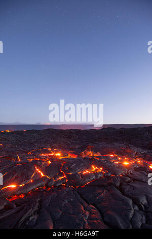 Sternen füllen den Himmel vor der Morgendämmerung als heiße Lava leuchtet durch die Ritzen der Pahoehoe in der Strömung 61 G, Hawaiʻi-Volcanoes-Nationalpark Stockfoto