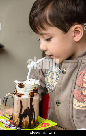 Ein kleiner Junge, trinken eine Tasse heiße Schokolade mit Schlagsahne gekrönt. Stockfoto