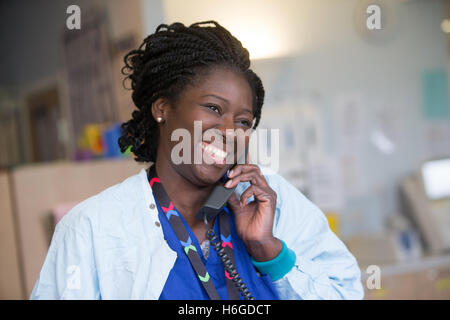 Eine glückliche Krankenschwester in einer Gemeinde im Chat über einen Patienten am Telefon Stockfoto