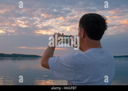 Mann am See fotografieren Sonnenaufgang mit Smartphone Stockfoto