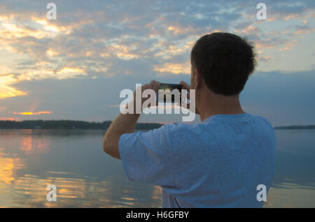 Mann am See fotografieren Sonnenaufgang mit Smartphone Stockfoto