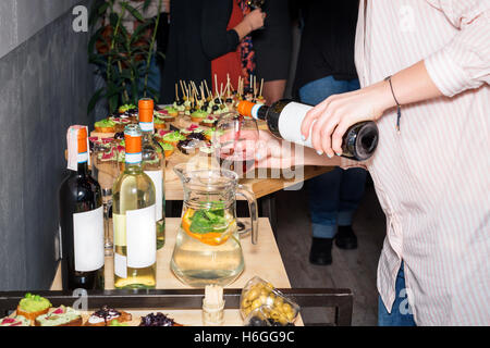 Kellner gießt Rotwein in einem Glas an einem Restauranttisch voller Vorspeisen mit Gästen stand in der Nähe. Stockfoto