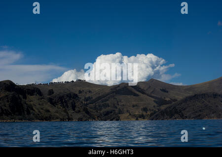 Auffallend weißen Wolken über einem Hügel mit Bäumen vor einem blauen Himmel am Titicacasee, Bolivien. Der See grenzt an Peru. Stockfoto