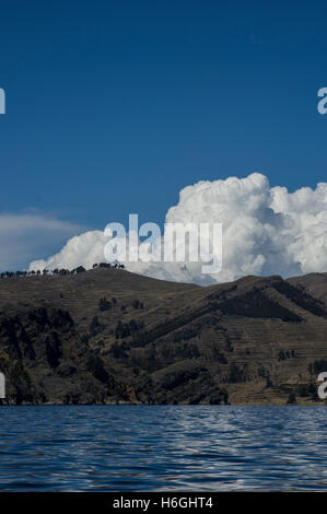 Auffallend weißen Wolken über einem Hügel mit Bäumen vor einem blauen Himmel am Titicacasee, Bolivien. Der See grenzt an Peru. Stockfoto