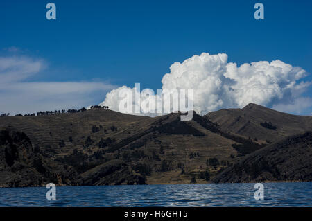 Auffallend weißen Wolken über einem Hügel mit Bäumen vor einem blauen Himmel am Titicacasee, Bolivien. Der See grenzt an Peru. Stockfoto