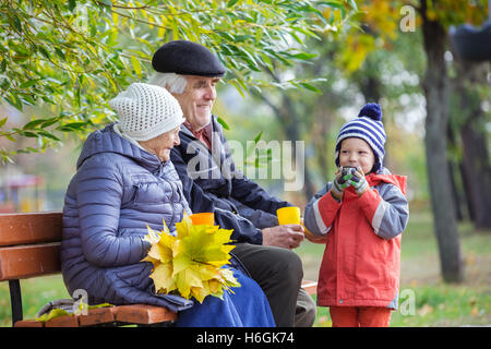 Älteres Paar und Enkel trinken heißen Tee im Herbst park Stockfoto