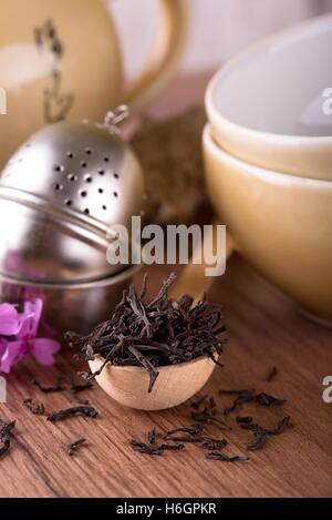 Vertikale Foto von trockenen Tee. Trockene Blätter auf Holzlöffel. Sieb nächsten zwei Tee-Set. Wasserkocher und zwei Schüsseln für chinesischen Tee. Rosa Stockfoto