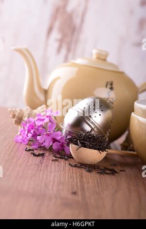 Vertikale Foto von trockenen Tee. Trockene Blätter auf Holzlöffel. Sieb nächsten zwei Tee-Set. Wasserkocher und zwei Schüsseln für chinesischen Tee. Rosa Stockfoto