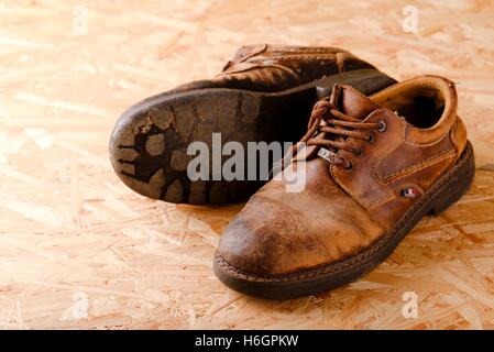 Horizontale Foto von zwei alten abgenutzten braune Lederschuhe mit beschädigten Schnürsenkel. Paar Stiefel ist auf OSB-Holzplatte gelegt. Einen Fußtritt geben ich Stockfoto