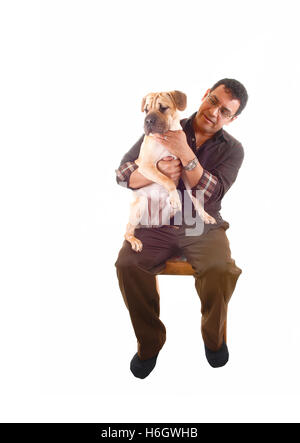 Ein Hispanic Mann in der braunen Kleidung auf einen Stuhl mit seinem besten Freund auf seinem Schoß sitzt, ein Sharpei Welpe für weißen Hintergrund. Stockfoto