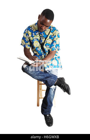 Ein hübscher junger schwarzer Mann sitzt und liest in einem Buch für den weißen Hintergrund. Stockfoto
