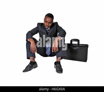 Ein schwarze Geschäftsmann mit Aktenkoffer auf seiner Seite sehr enttäuscht über weißem Hintergrund auf dem Boden sitzen. Stockfoto